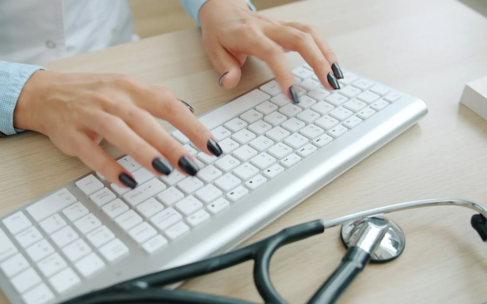 Hands typing on a keyboard beside a stethoscope